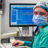 Emily Bludov, a certified registered nurse anesthetist (CRNA), looks up from an anesthesia machine in an operating room at Atrium Health’s Carolina’s Medical Center.